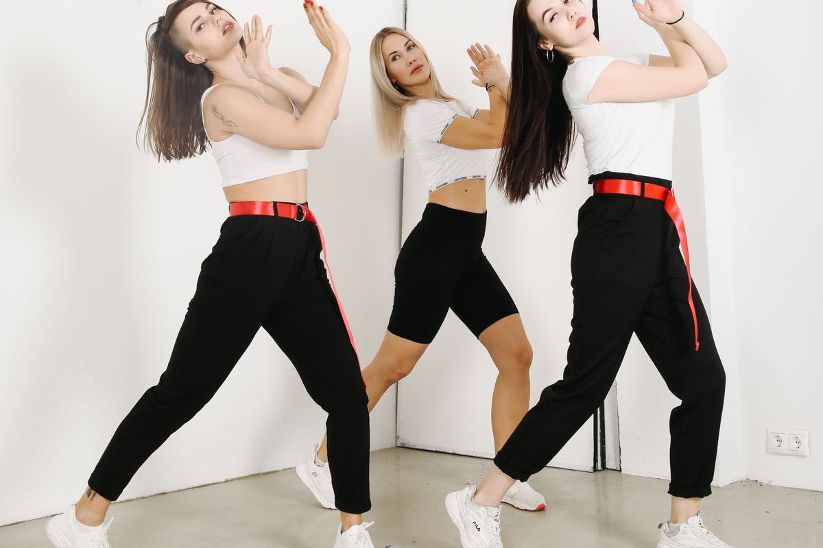白いスタジオでK-POPの振り付けをそろえて踊る3人の女性